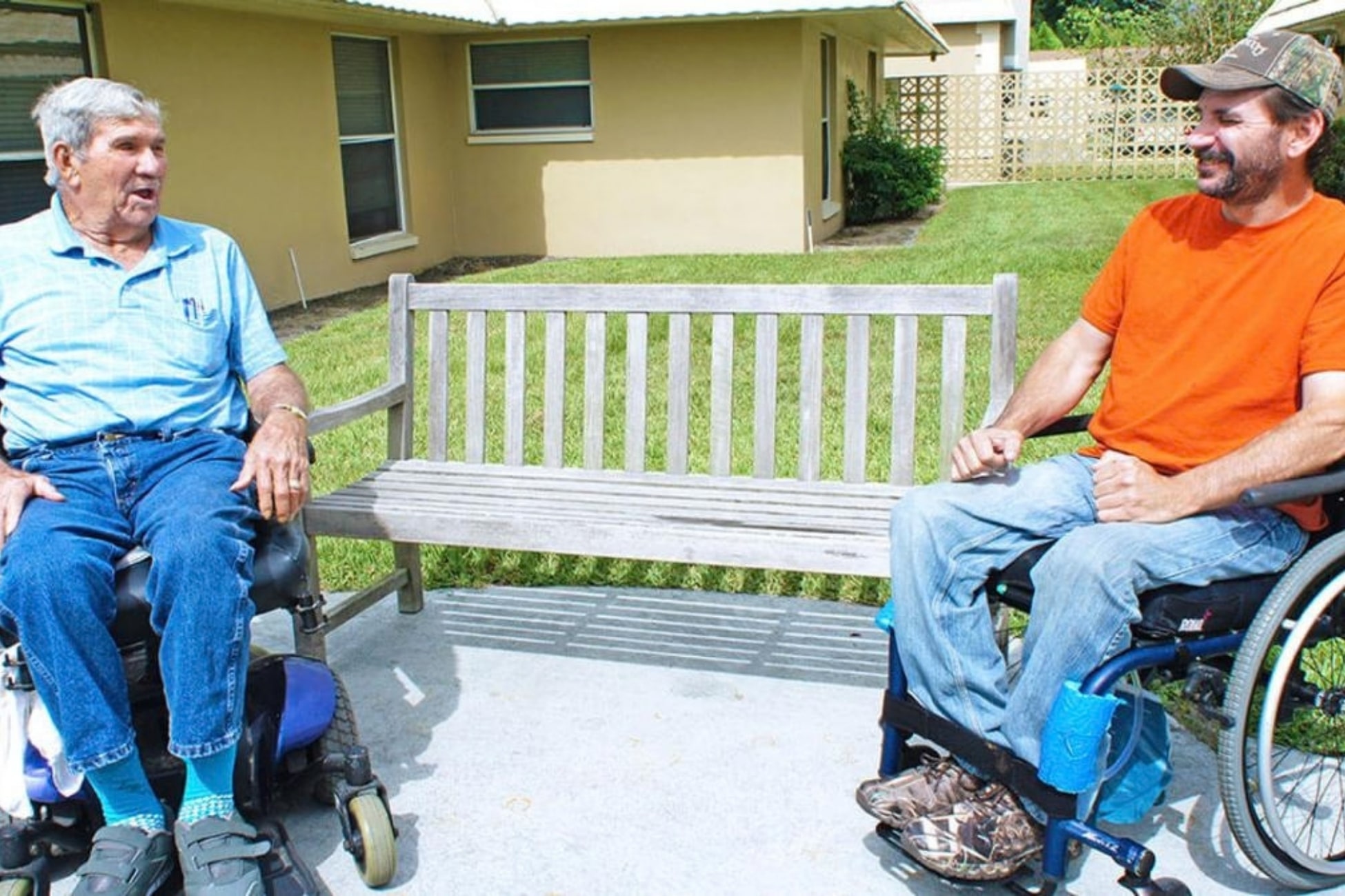 Two residents using wheelchairs visit in the outdoor courtyard.